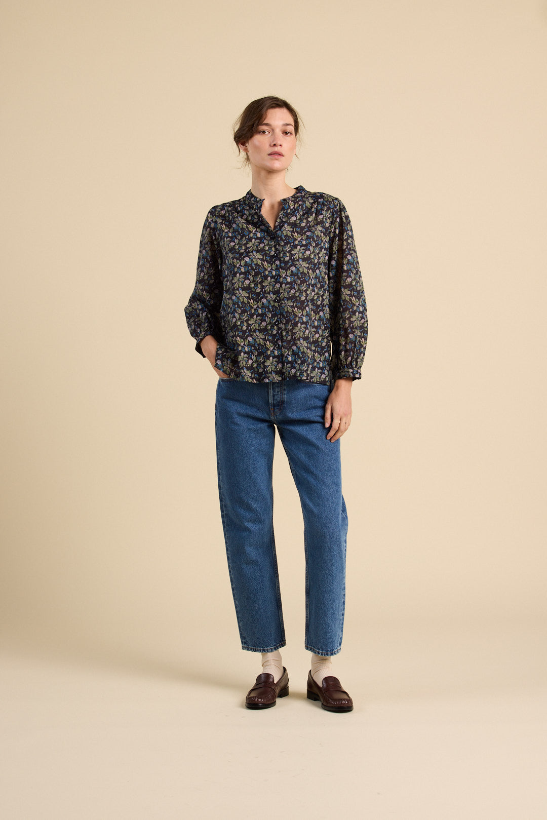 Woman wearing a patterned blouse and blue jeans on a beige background