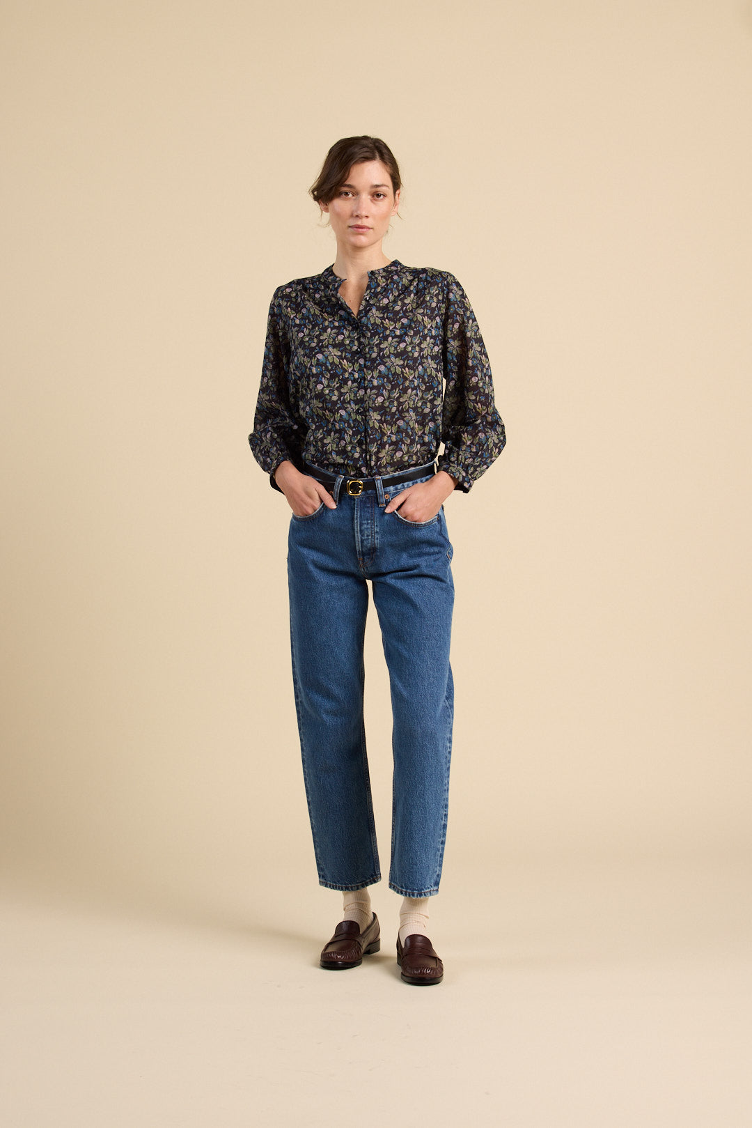 Woman wearing a patterned shirt and blue jeans on a beige background