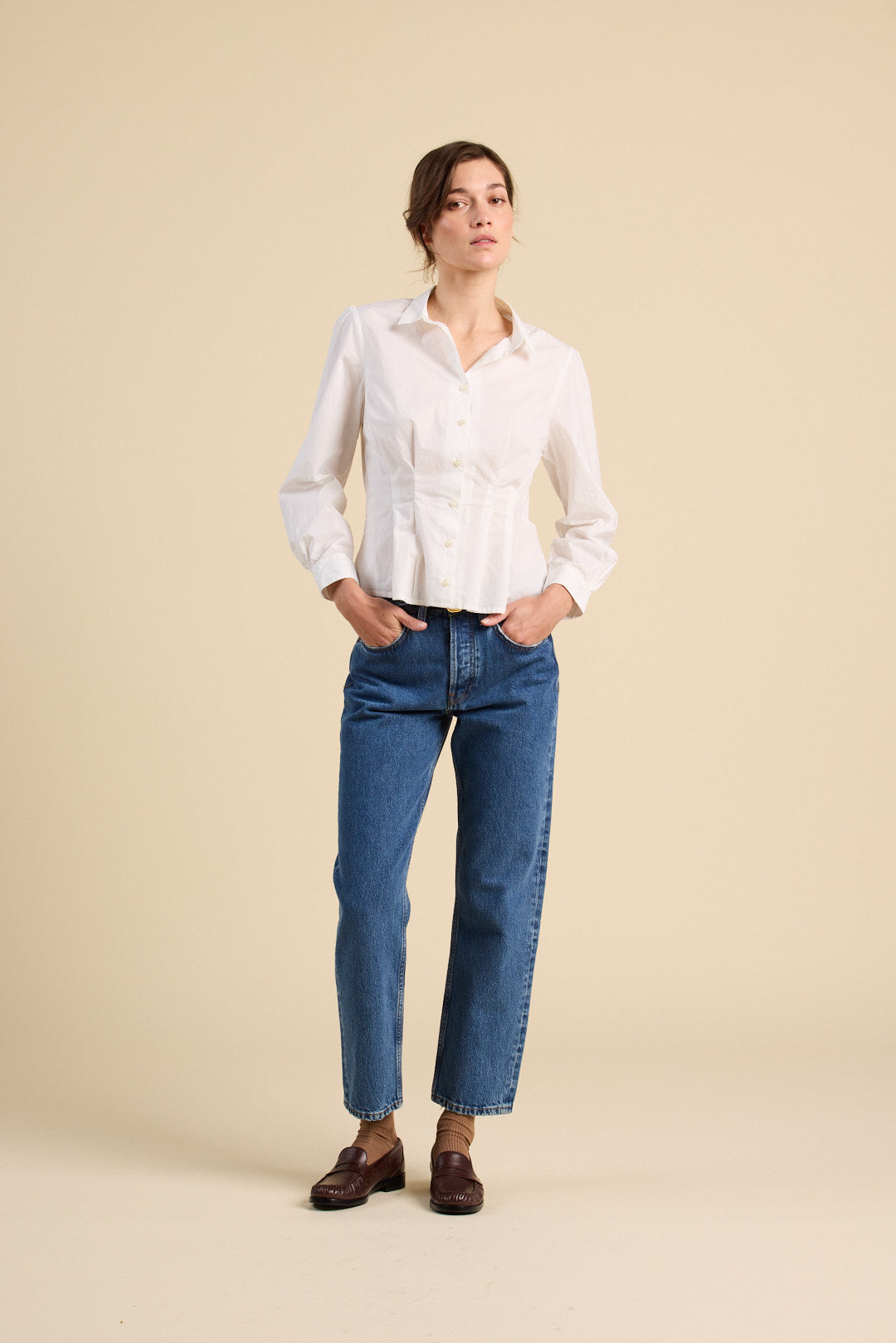 Woman wearing a white blouse and blue jeans against a beige background