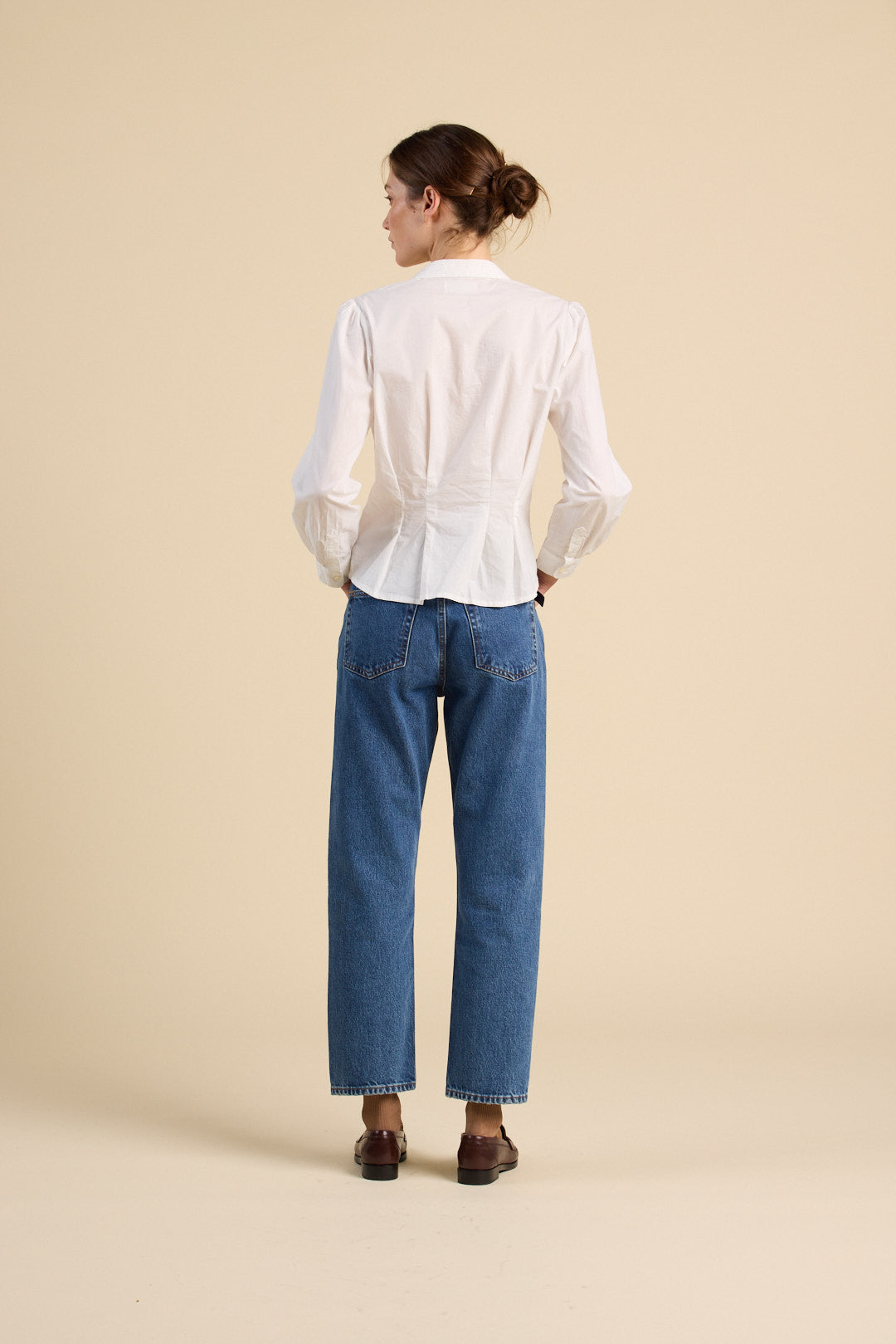 Woman wearing a white blouse and blue jeans on a beige background
