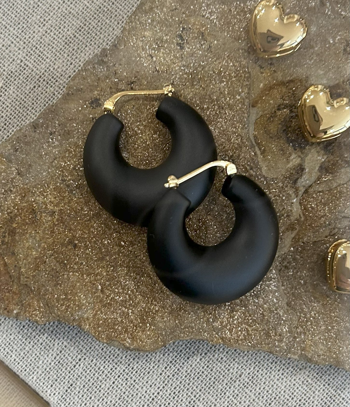 Black hoop earrings on a textured surface with gold heart-shaped objects.