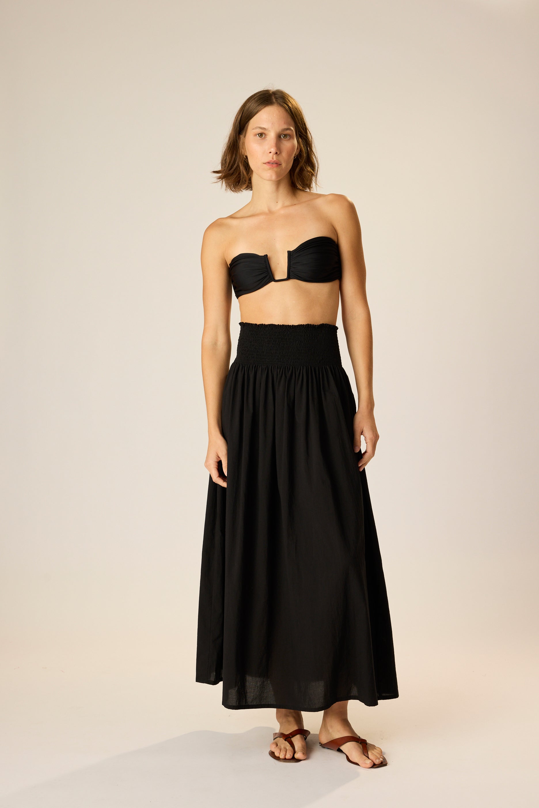 Woman wearing a black strapless top and long black skirt on a plain background