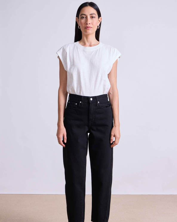 Woman wearing a white top and black pants against a plain background