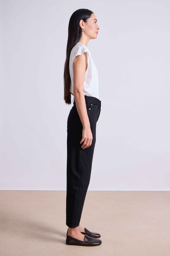 Woman wearing a white top and black pants standing against a plain background