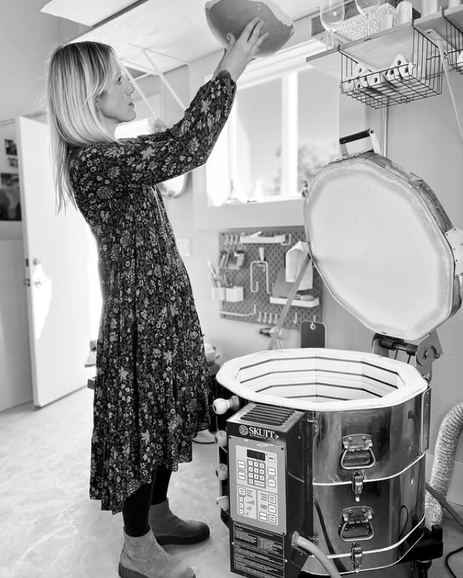 Person interacting with a large machine, possibly an oven or kiln, in a workshop setting.