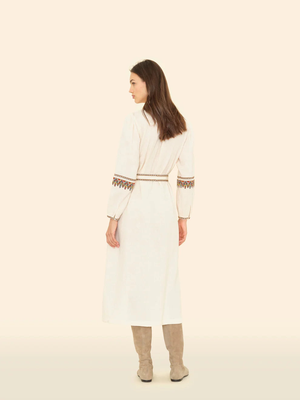 Woman wearing a long, light-colored dress with intricate patterns on a beige background