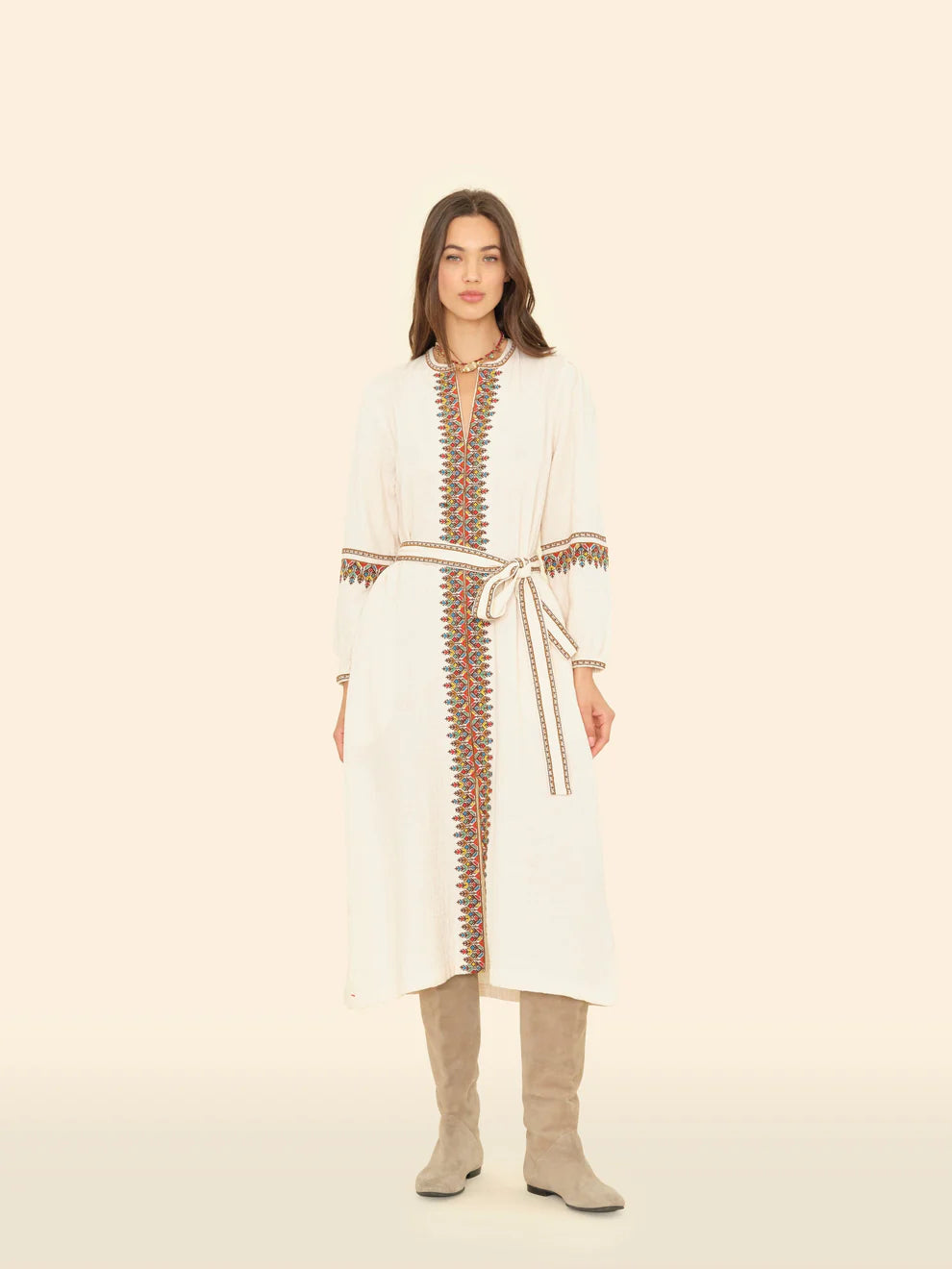 Woman wearing a white dress with brown embroidery on a beige background