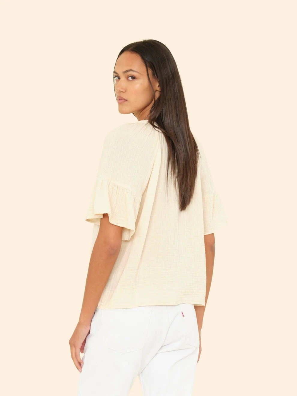 Woman wearing a light-colored top and white pants on a beige background