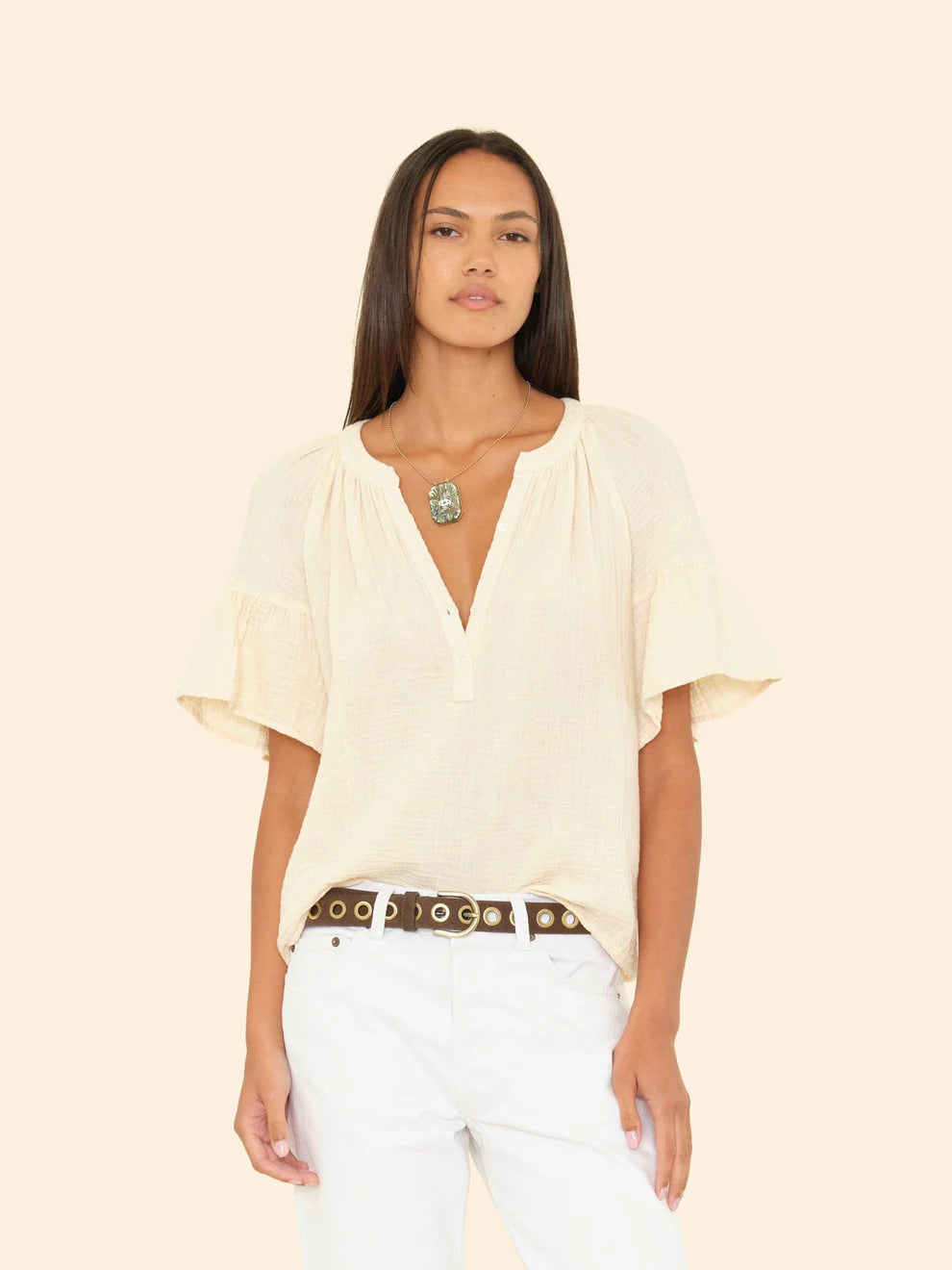 Woman wearing a beige blouse and white pants with a belt on a beige background