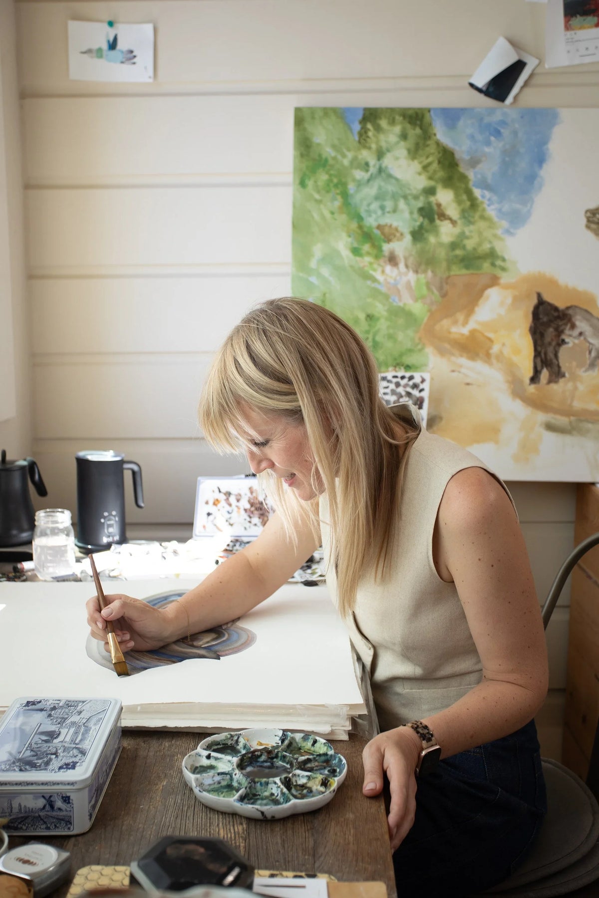 Artist Cristina Hobbs painting a watercolor landscape at her studio desk