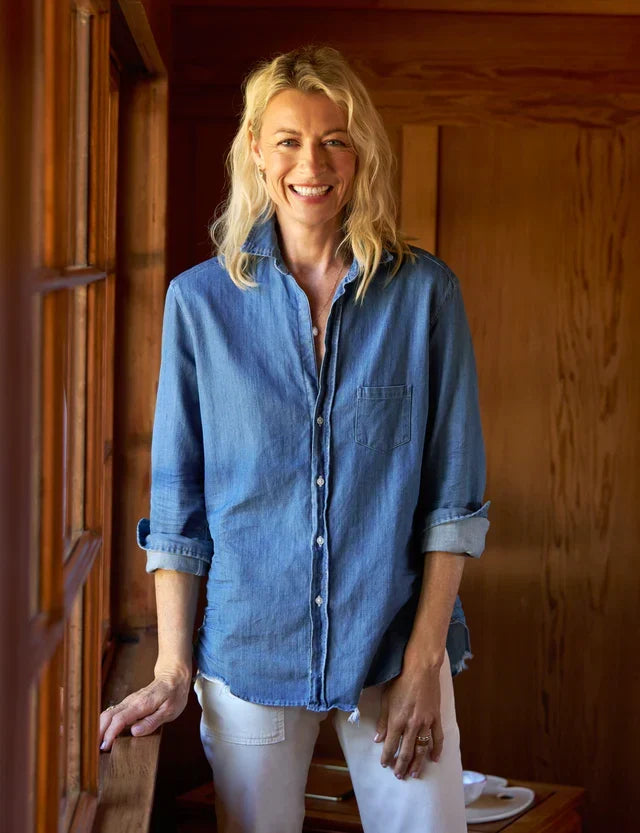 Smiling woman wearing a chambray button-down shirt with white trousers indoors