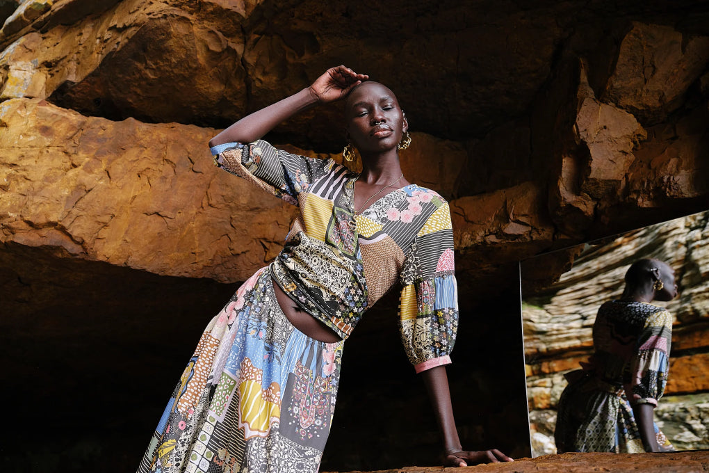 Model in patchwork-print Asha Eleven dress posing inside a sunlit rock cave