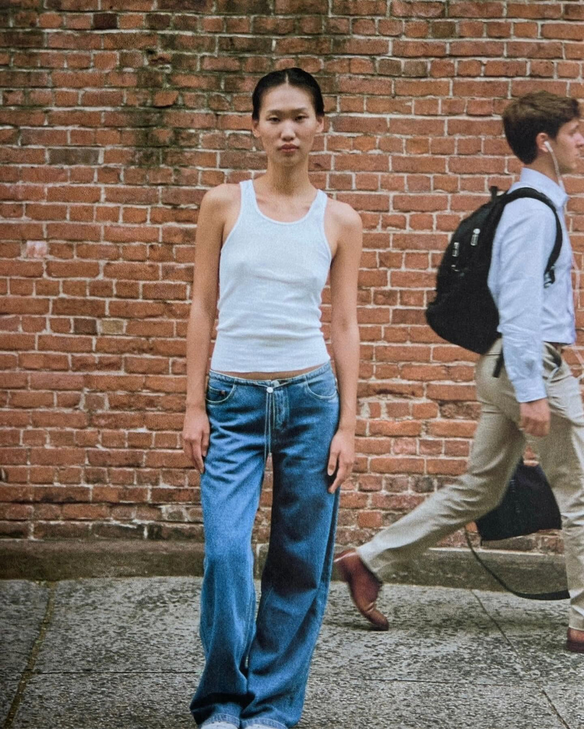 Woman in white tank top and wide-leg jeans standing against brick wall