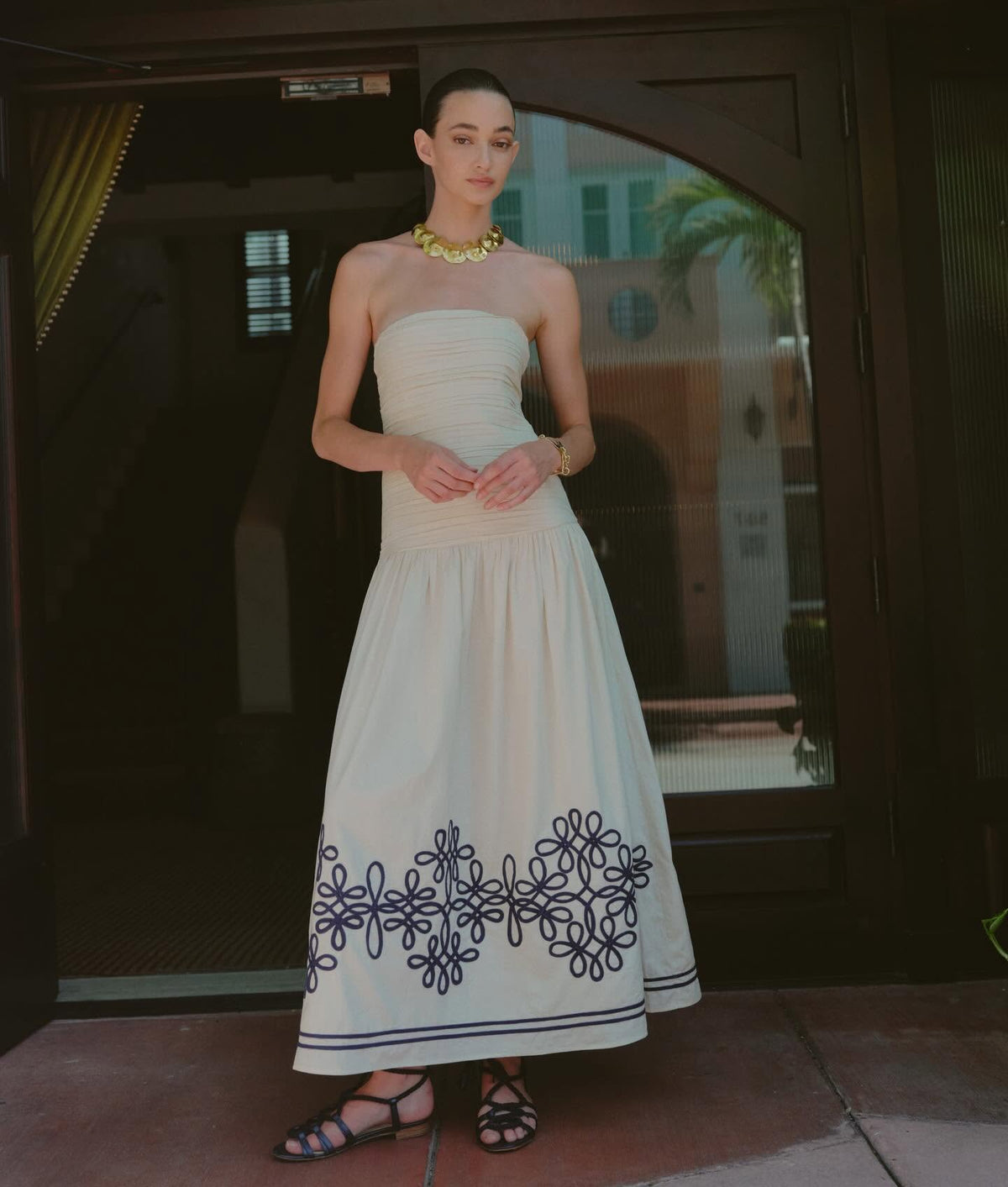 Strapless cream maxi dress with navy embroidered hem, styled with gold necklace