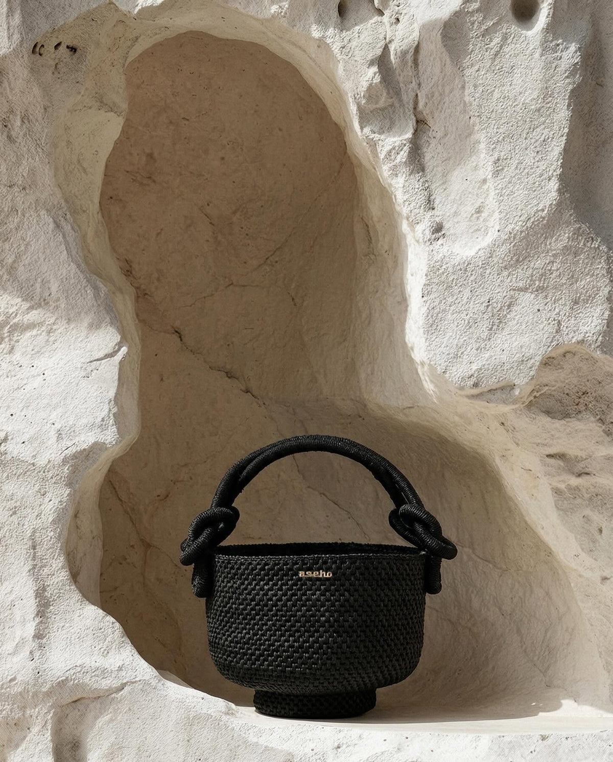 Aseho woven raffia basket bag with knotted rope handle in carved stone niche