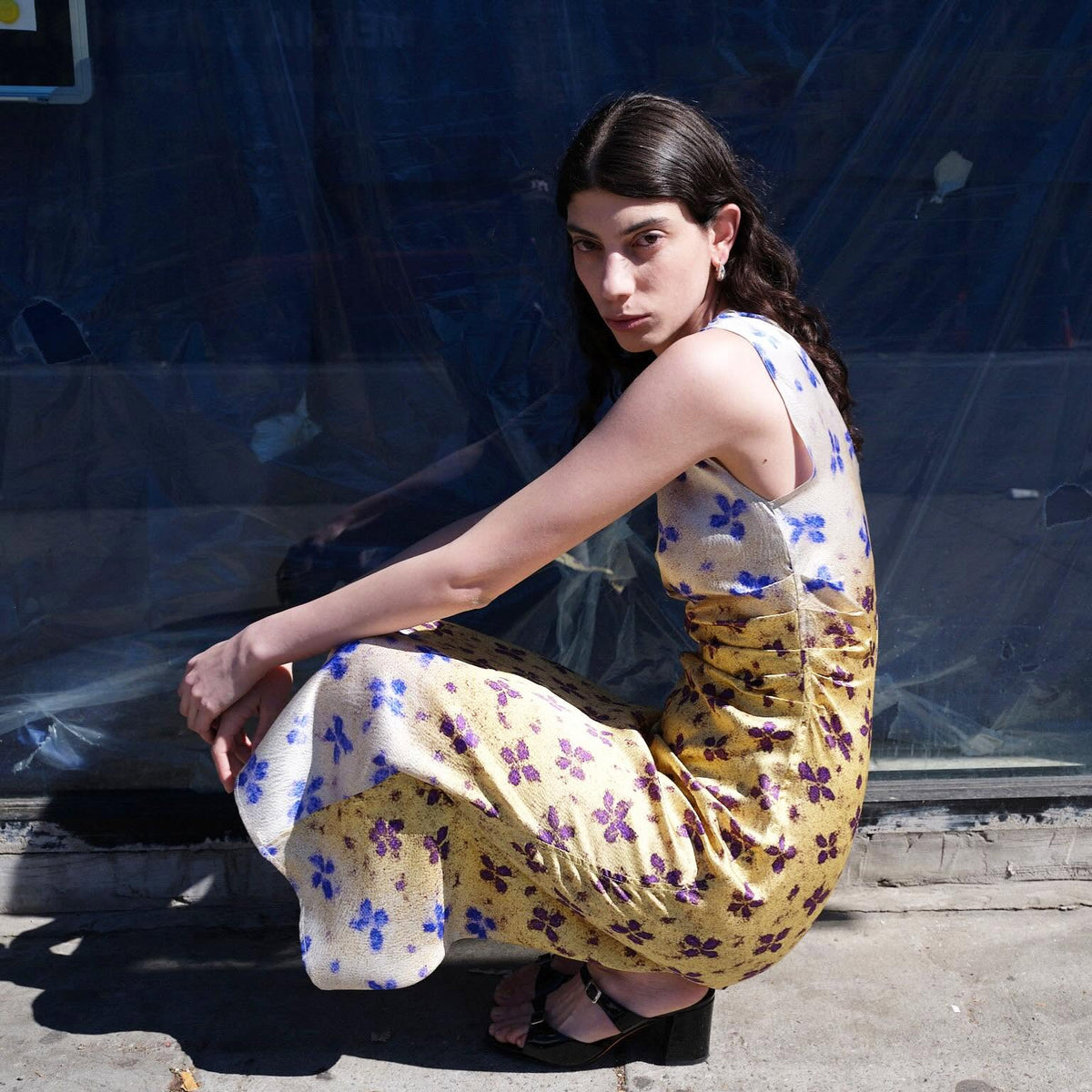 Woman crouching in a sleeveless yellow floral No.6 dress with purple sandals