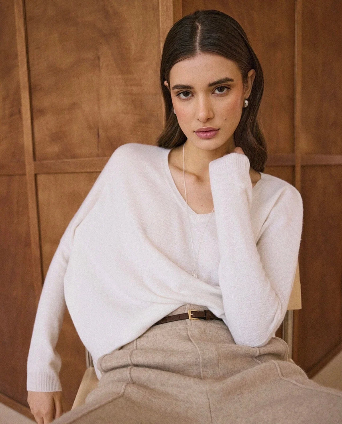 Woman in white V-neck cashmere sweater over beige trousers with a thin belt