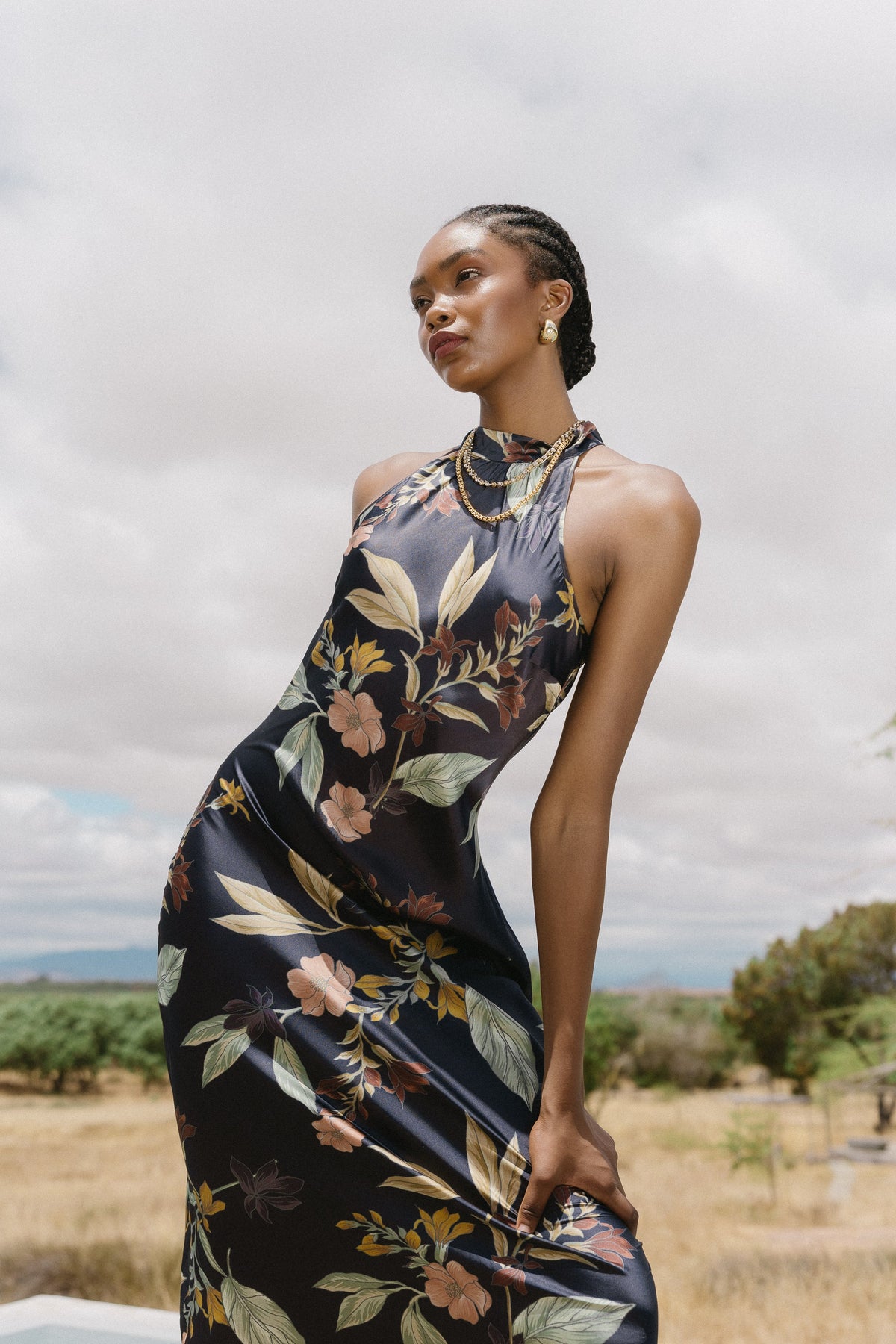 Woman in sleeveless floral maxi dress standing in an open field under clouds