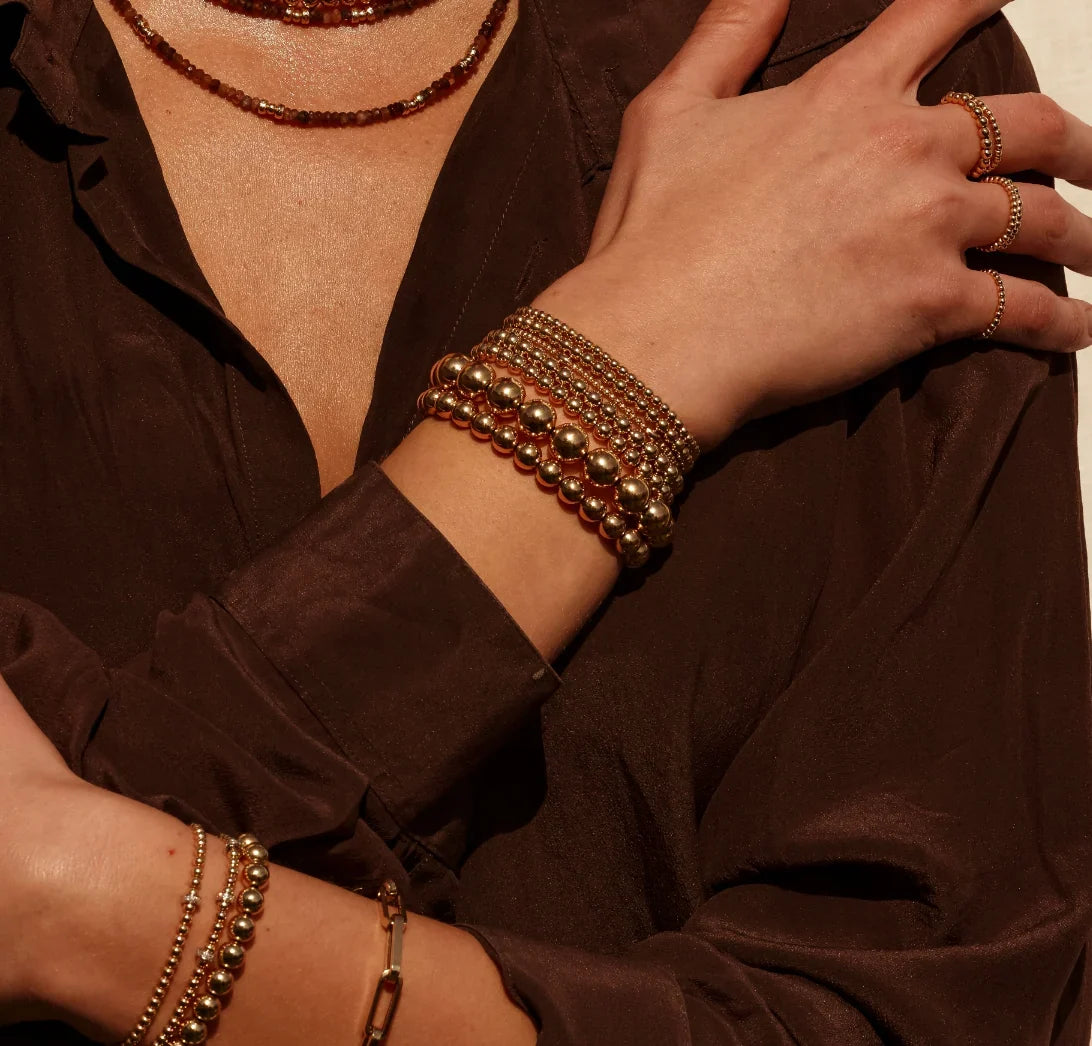 Model wearing stacked gold-filled beaded bracelets, rings, and beaded necklace