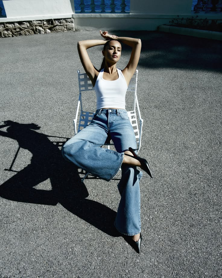 Woman in white tank and wide-leg jeans lounges on a chair outdoors