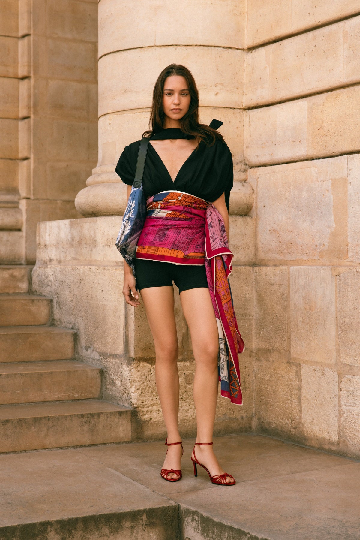Model wears black top and shorts with a pink printed scarf tied at the waist