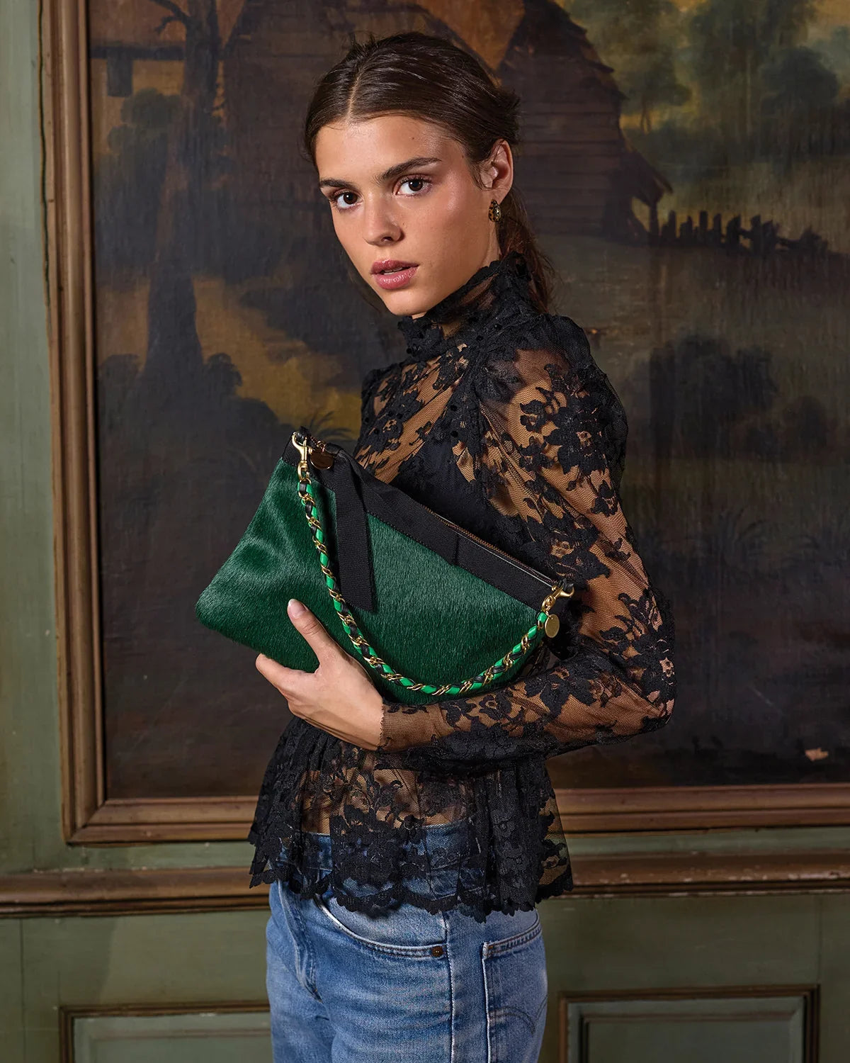 Woman in black lace top holding a green calf-hair clutch with chain strap