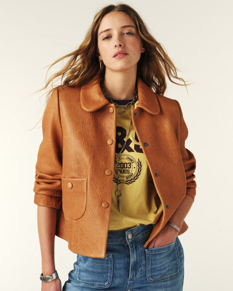 Woman wearing a brown jacket, yellow graphic t-shirt, and blue jeans on a white background