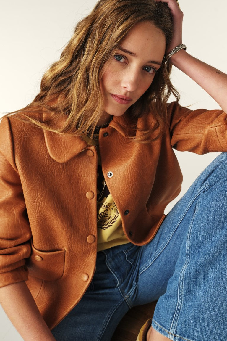 Woman wearing a brown jacket and blue jeans against a plain background