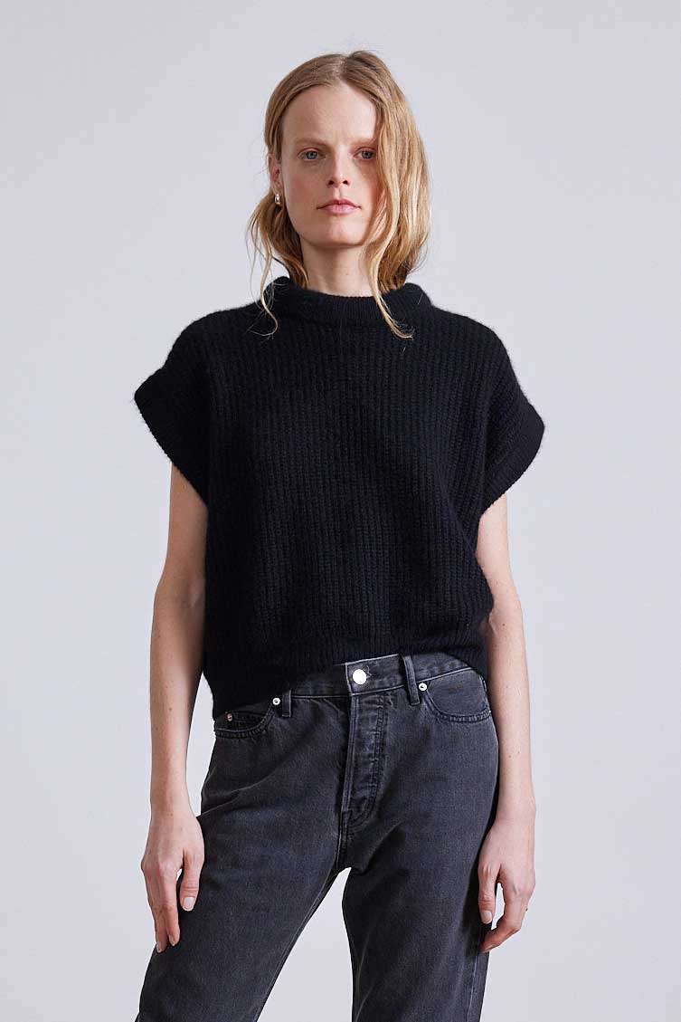 Person wearing a black sweater and dark jeans on a plain background
