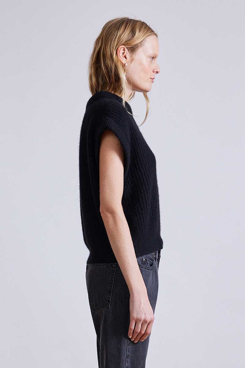 Person wearing a black sleeveless sweater against a light gray background