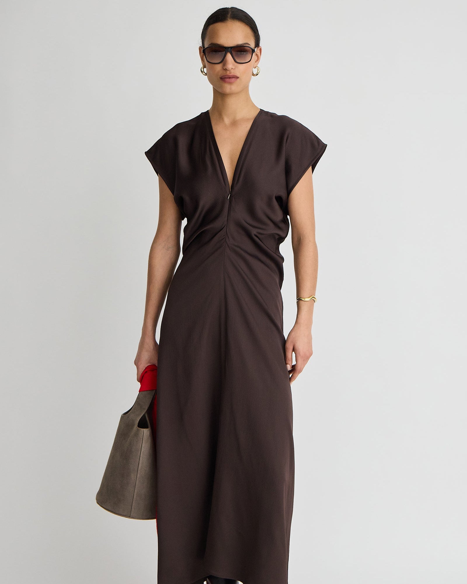 Woman wearing a brown dress holding a matching handbag against a white background