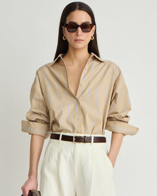 Woman wearing a beige striped shirt and white pants with sunglasses on a plain background