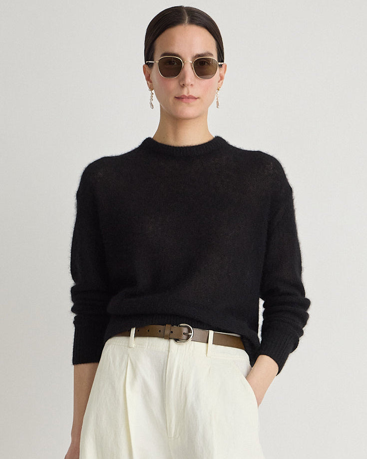 Woman wearing a black sweater and white pants with sunglasses on a plain background