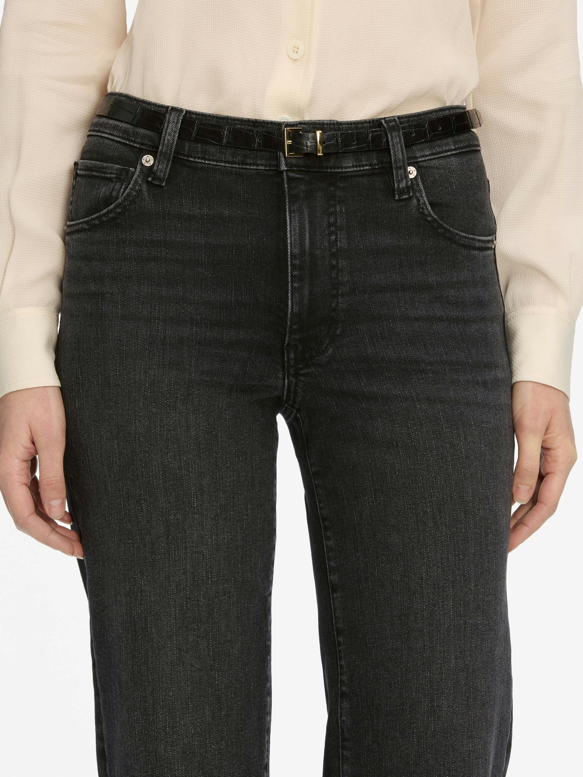 Person wearing black jeans with a beige shirt on a white background