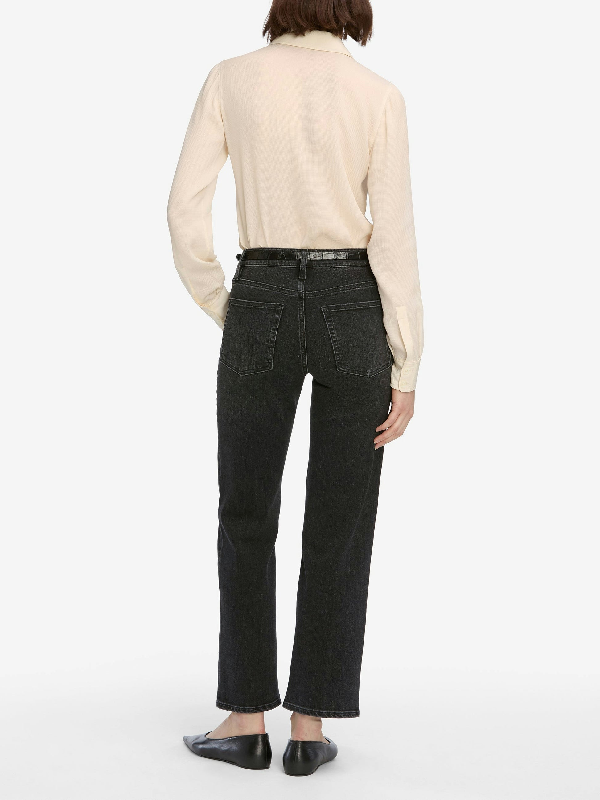 Person wearing black jeans and a beige shirt on a white background