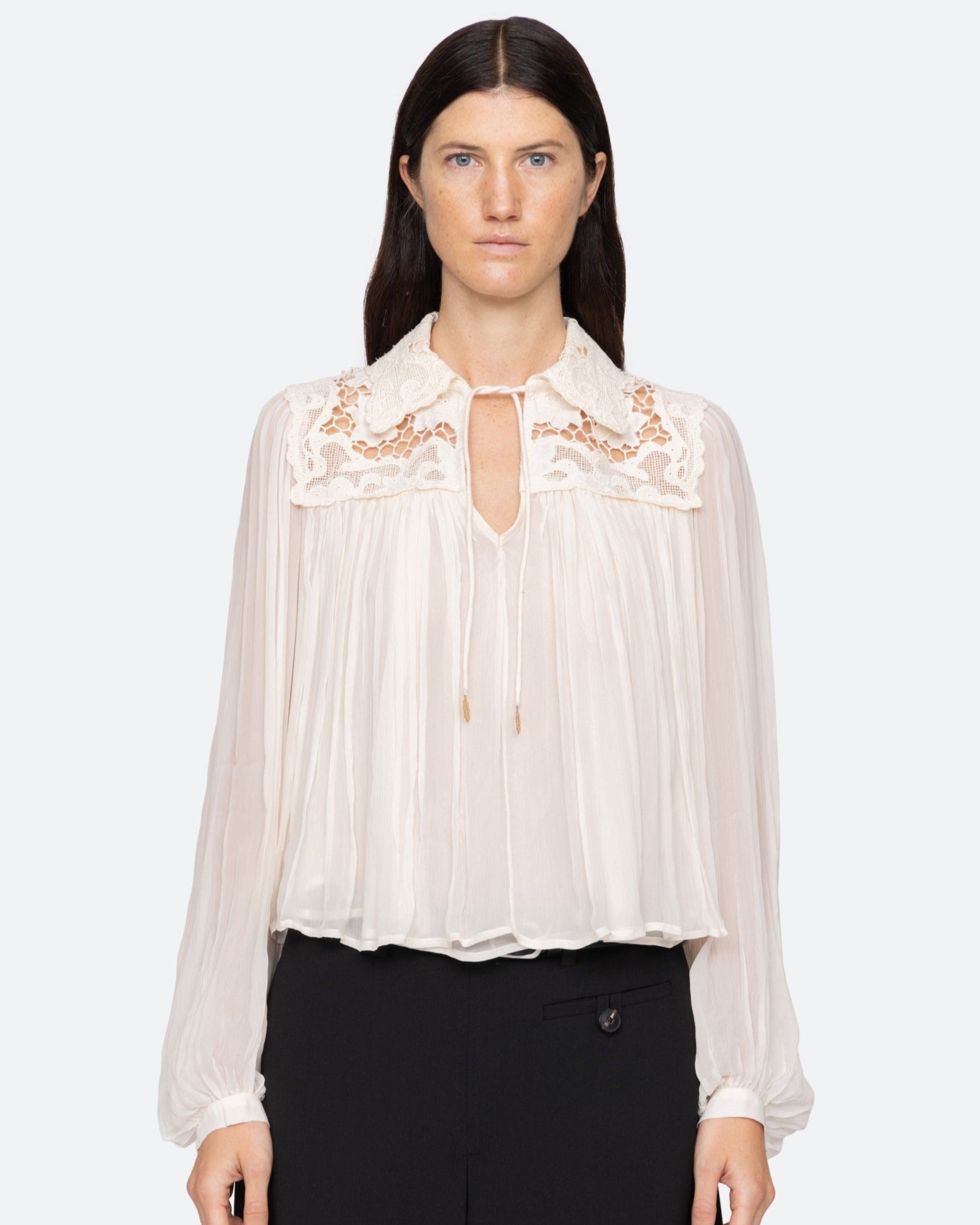 Woman wearing a white blouse with lace details on a white background