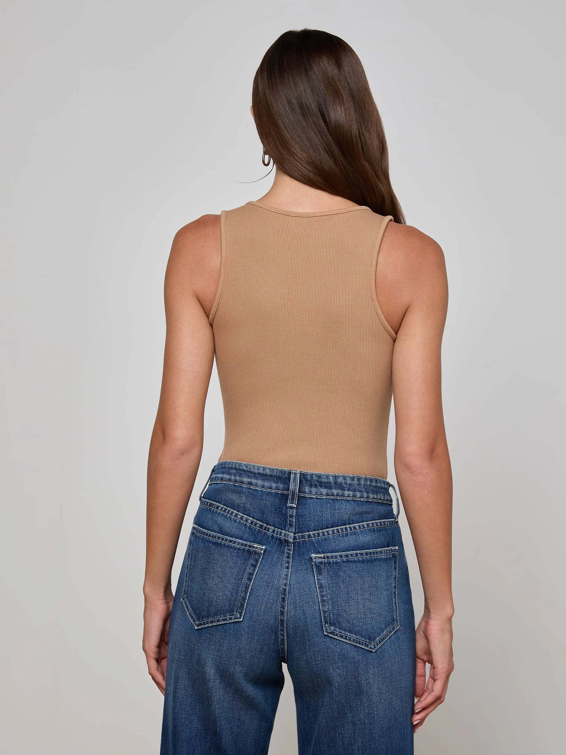 Person wearing a beige tank top and blue jeans on a plain background