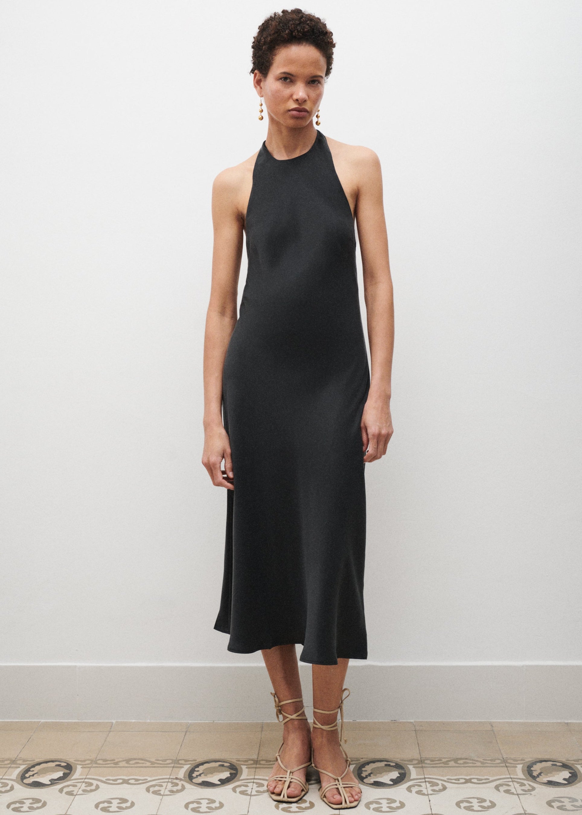 Woman wearing a black sleeveless dress against a white wall.