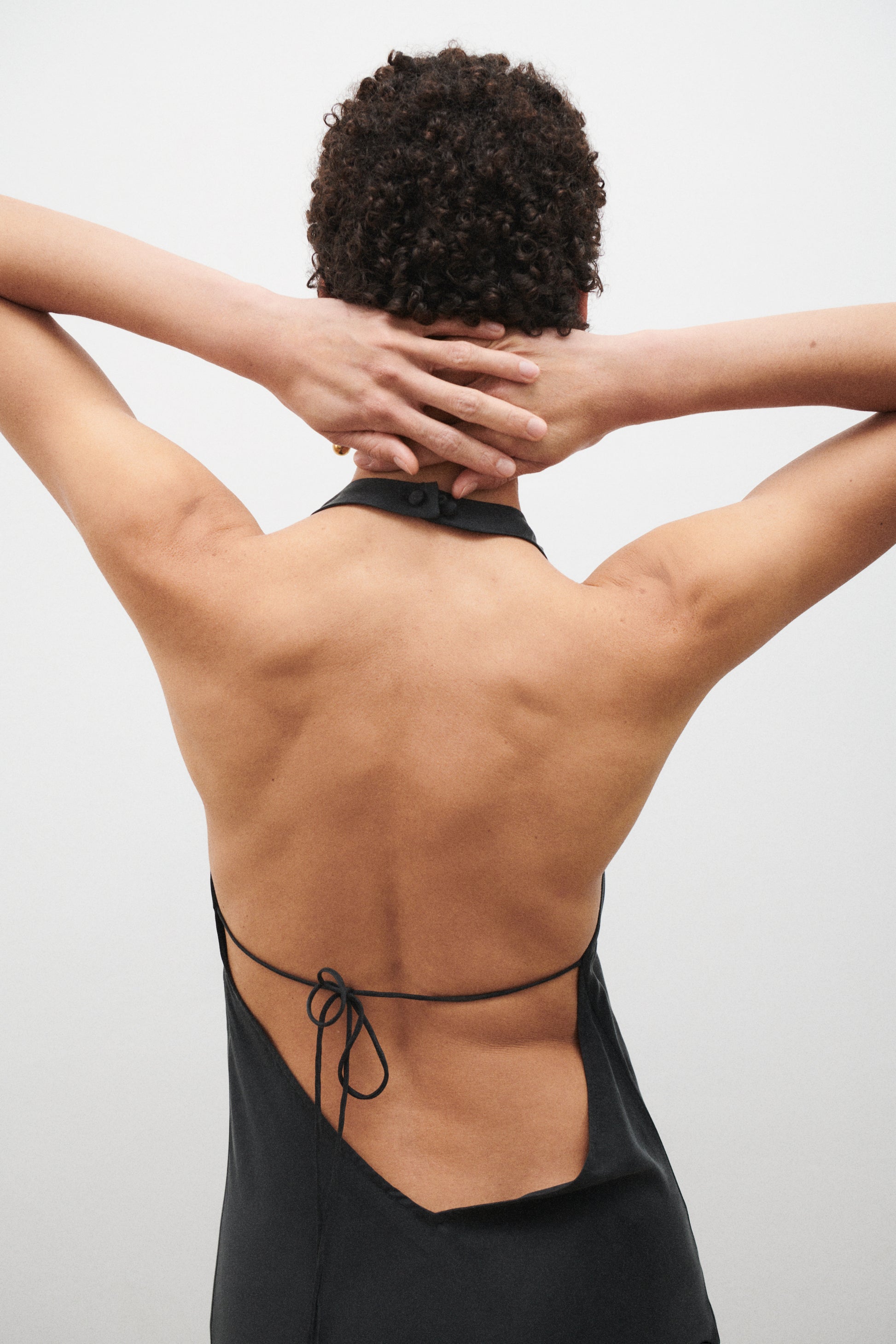 Person wearing a black dress with an open back against a light gray background