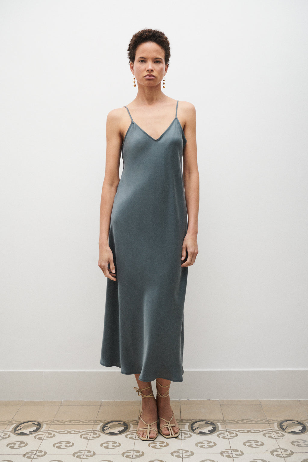 Woman wearing a blue satin slip dress standing against a white wall.