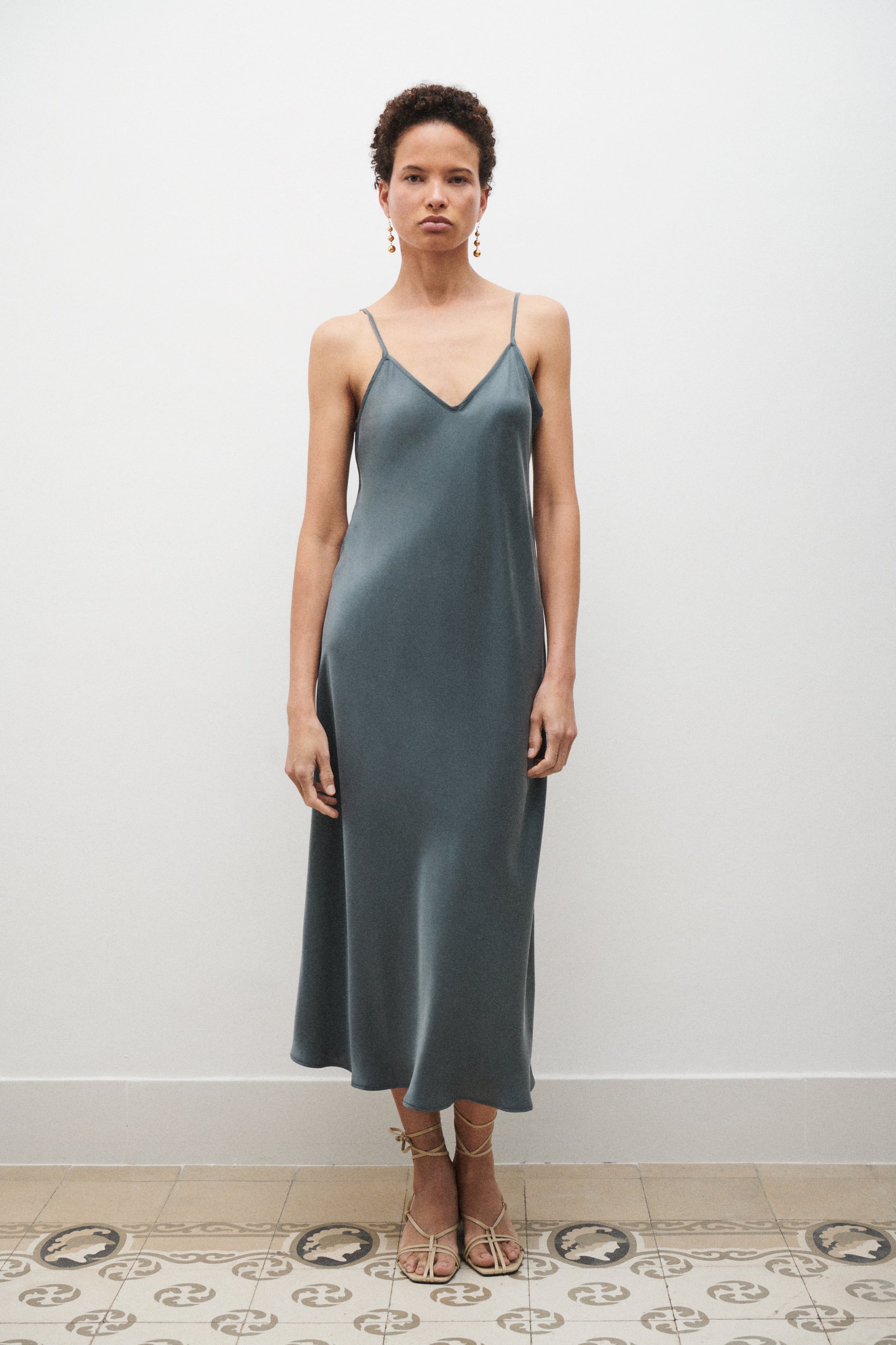 Woman wearing a blue satin slip dress standing against a white wall.