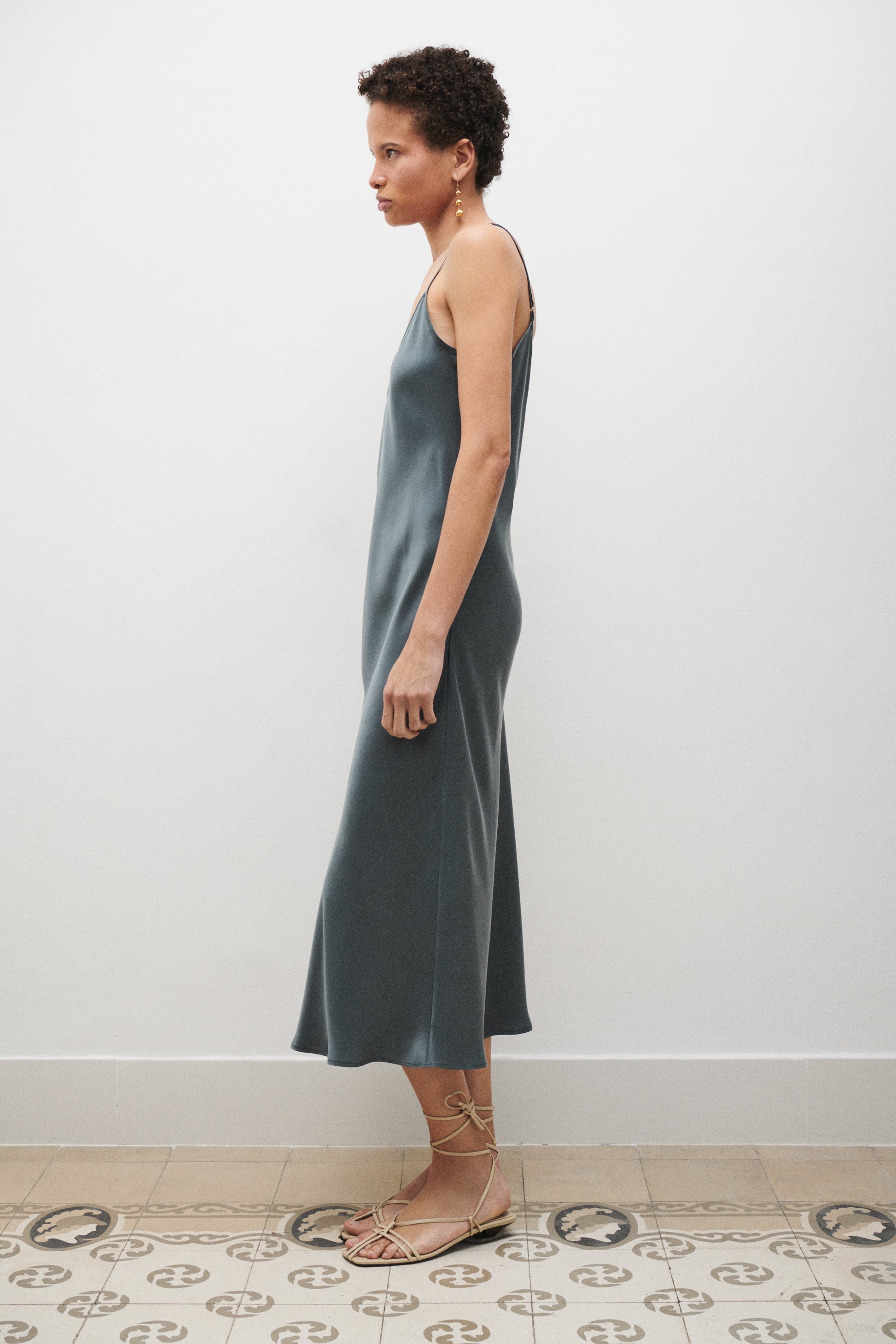 Woman wearing a teal slip dress standing against a white wall.