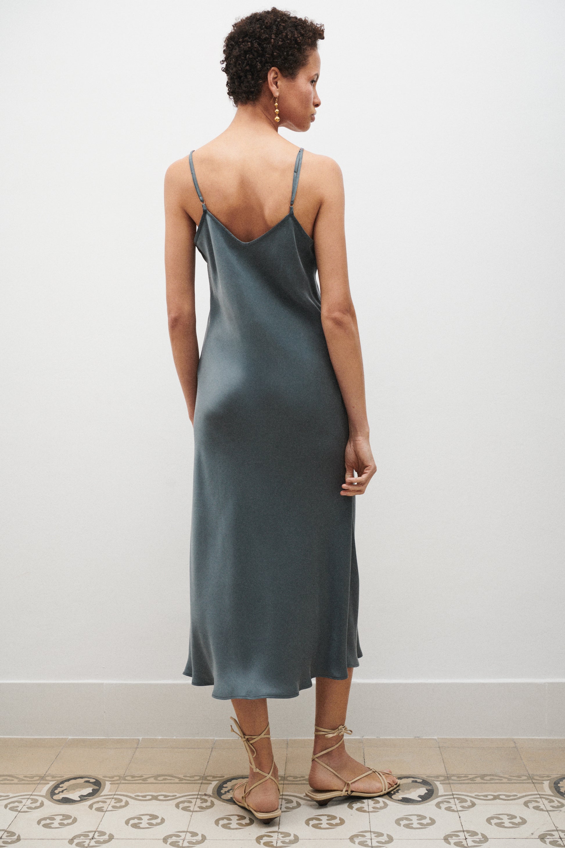 Woman wearing a light blue slip dress standing against a white wall.