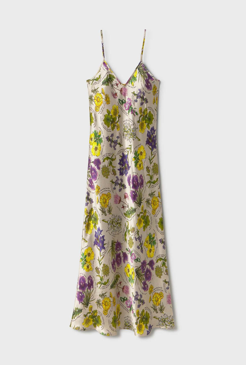 A sleeveless floral print slip dress with thin spaghetti straps, featuring a vibrant pattern of yellow, purple, and green flowers on a light beige background, shown against a plain light gray studio backdrop.