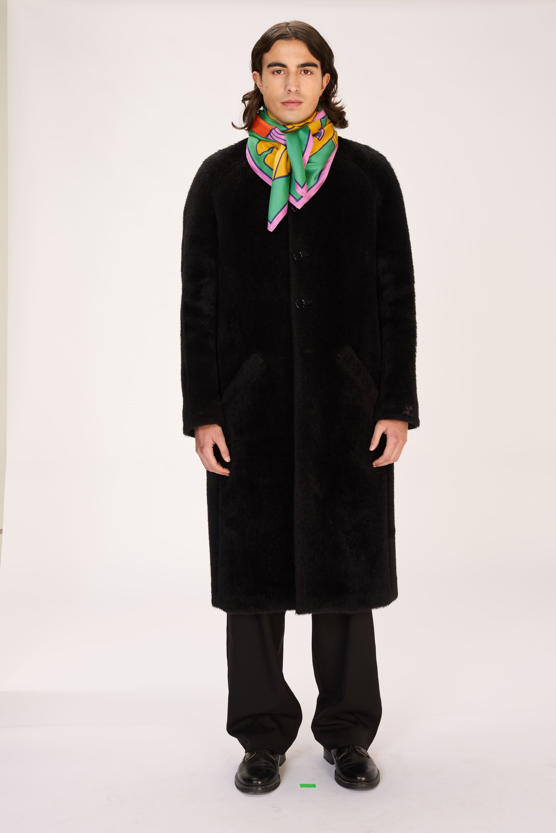 Person wearing a black coat and colorful scarf on a white background