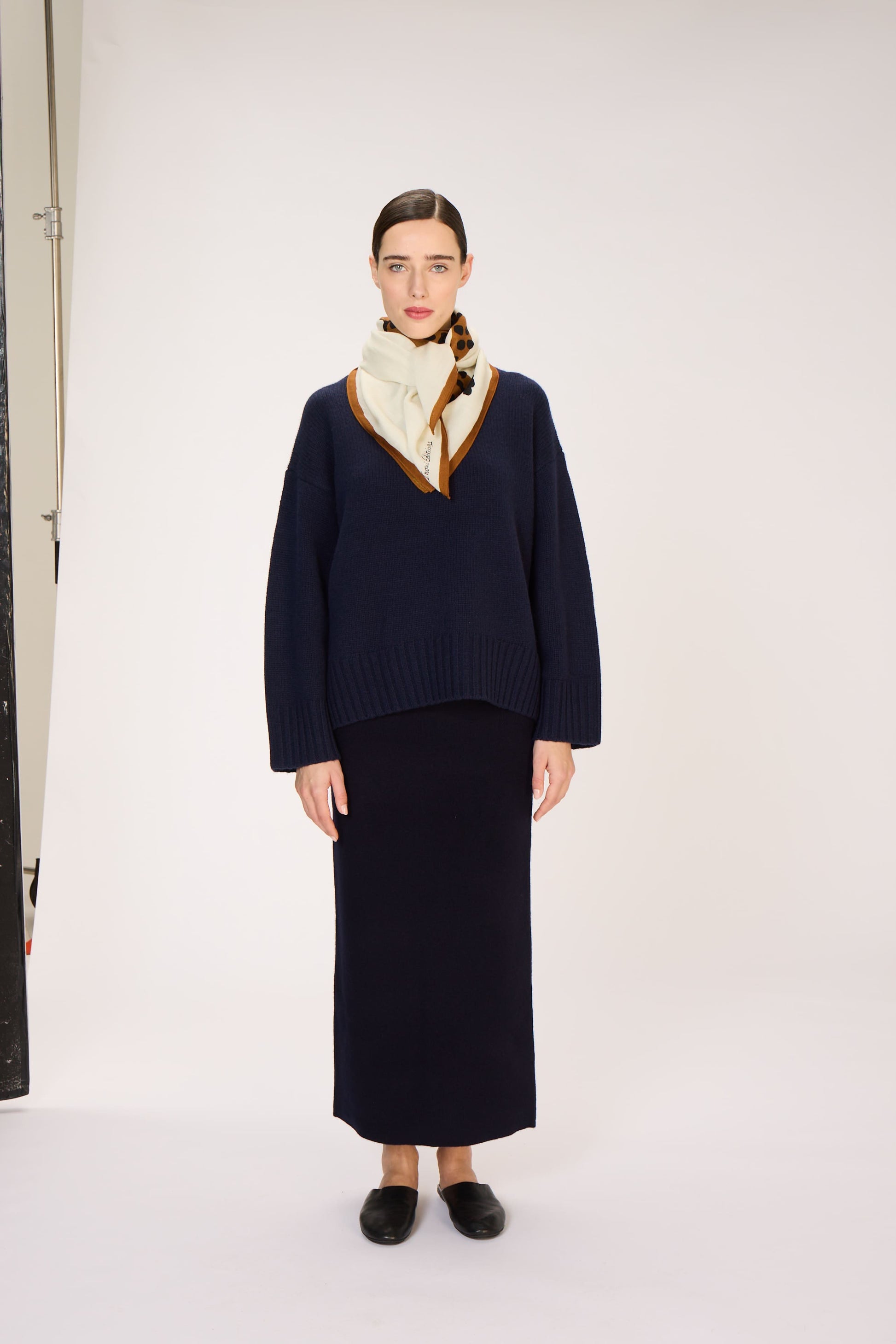 Person wearing a navy sweater and skirt with a beige scarf against a white background