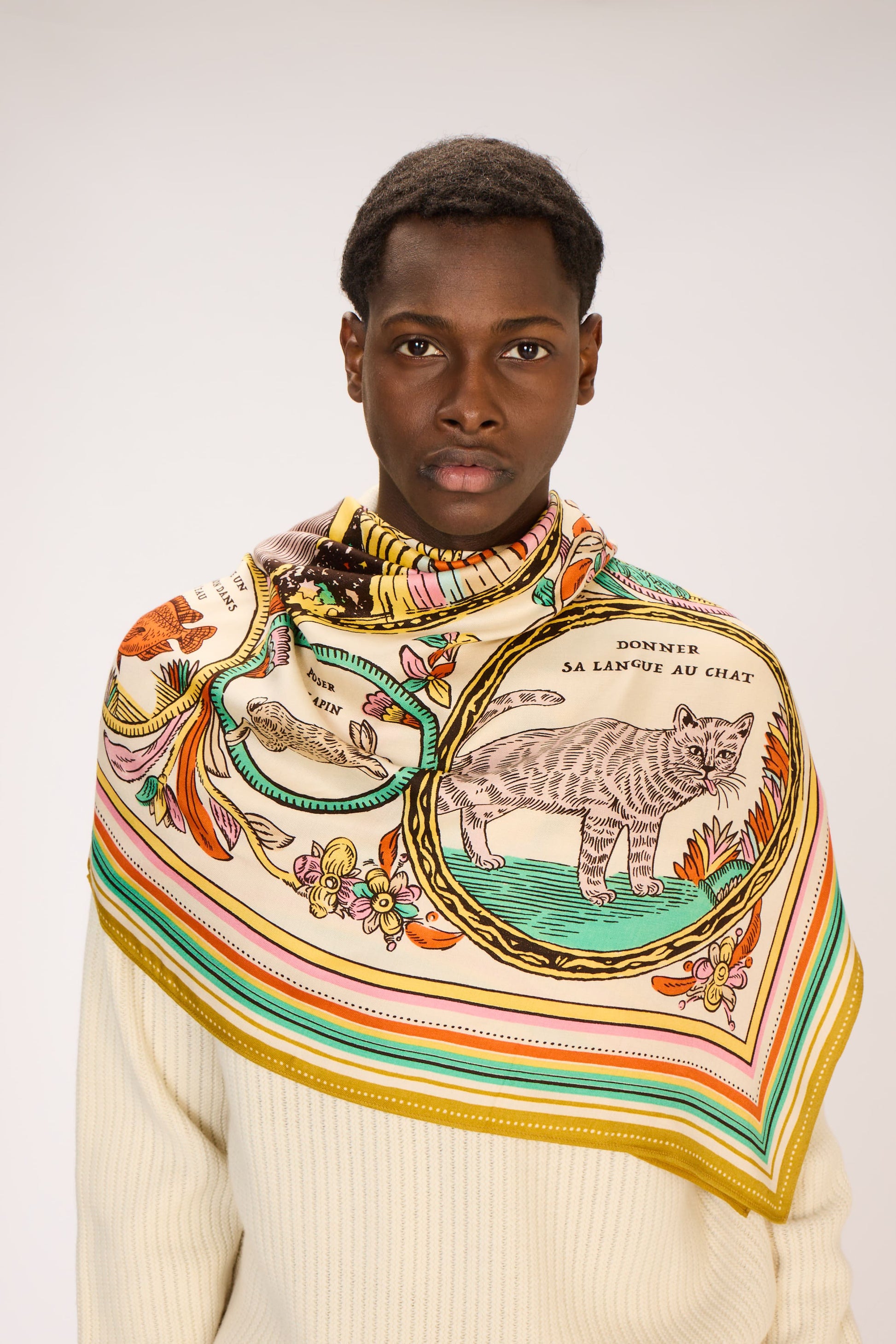 Person wearing a colorful patterned scarf with a cat design on a plain background
