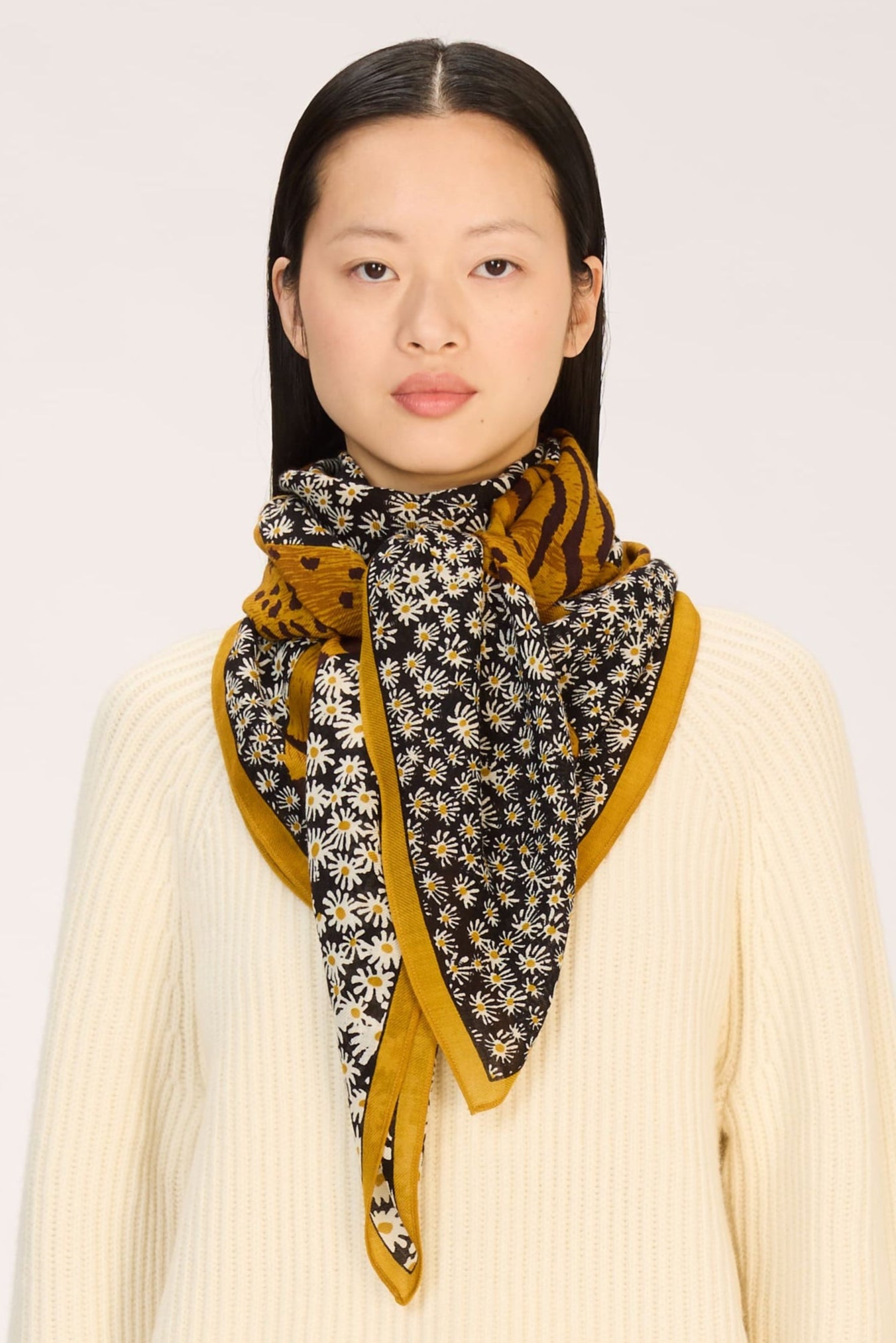 Person wearing a cream outfit with a patterned scarf on a white background