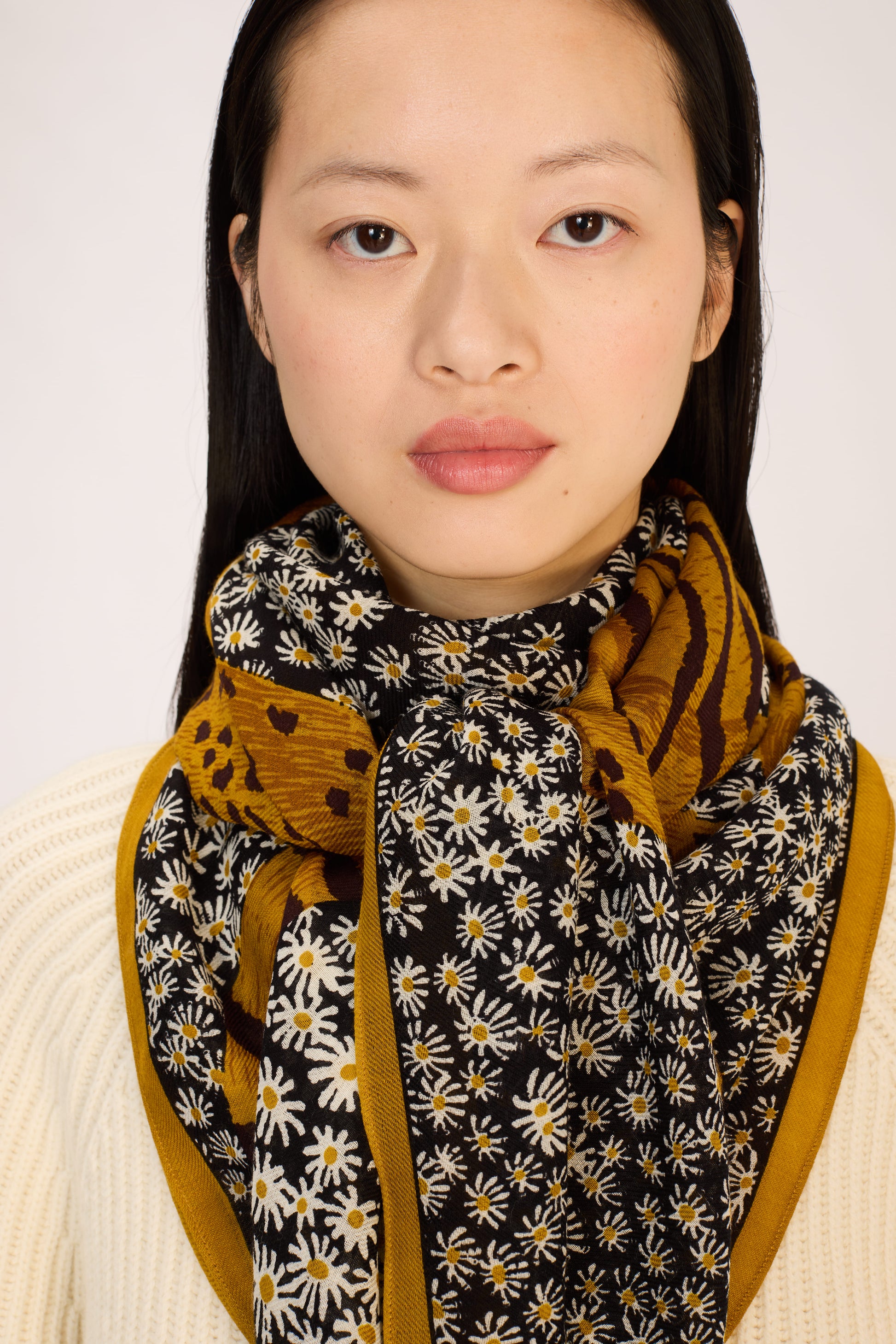 Woman wearing a floral scarf with mustard yellow accents on a plain background