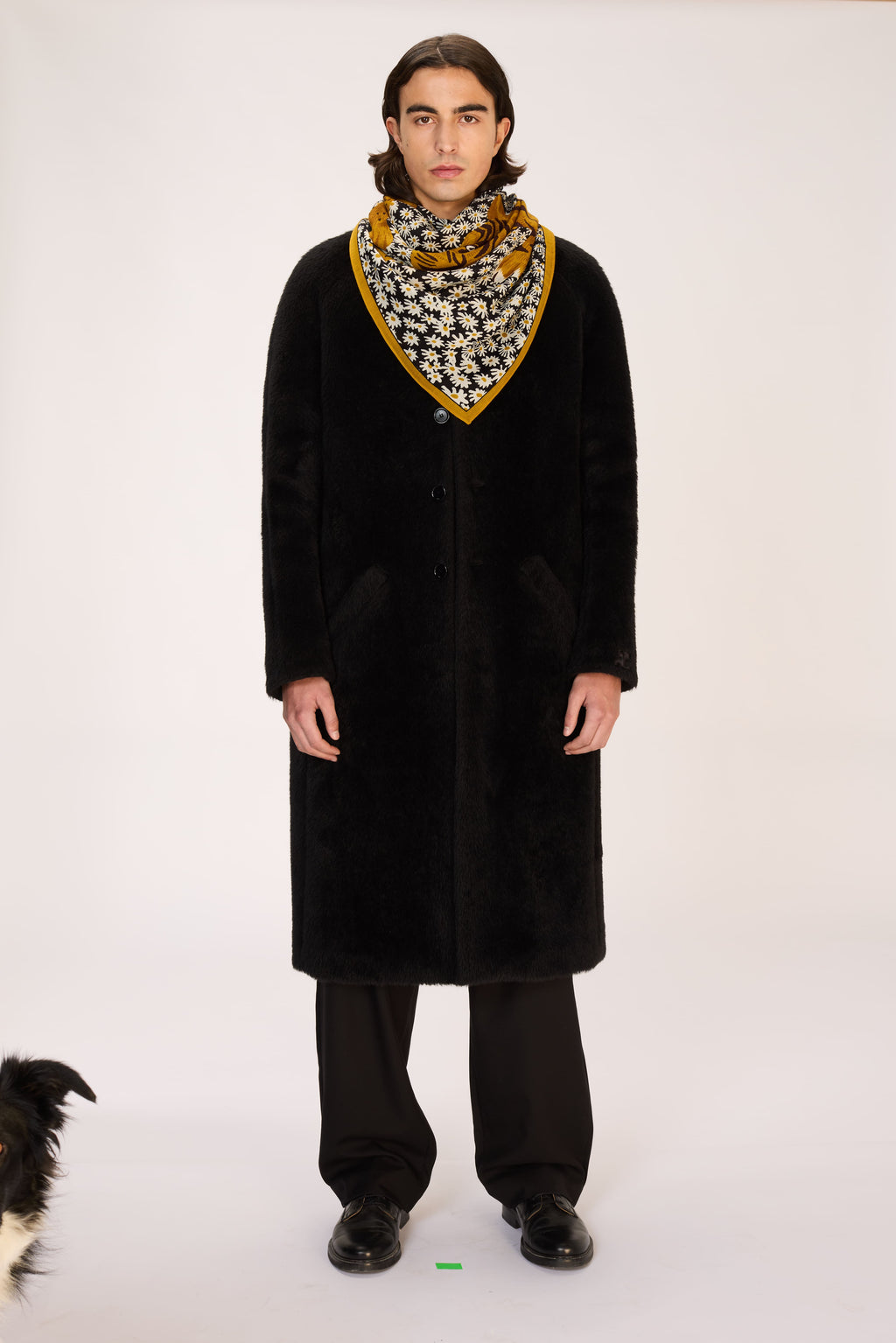 Person wearing a long black coat and patterned scarf on a white background